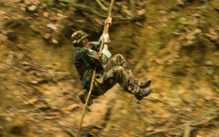 an image of a brave man dressed in camouflage swinging on a vine in the Guyanan jungle