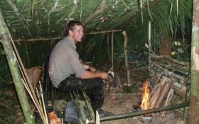 an image of a man sitting in a shelter he built himself during a Bushmasters jungle survival course.