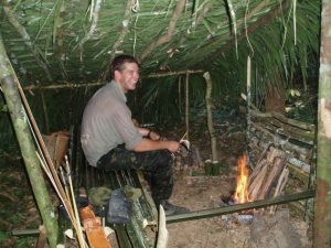 an image of a man sitting in a shelter he built himself during a Bushmasters jungle survival course.
